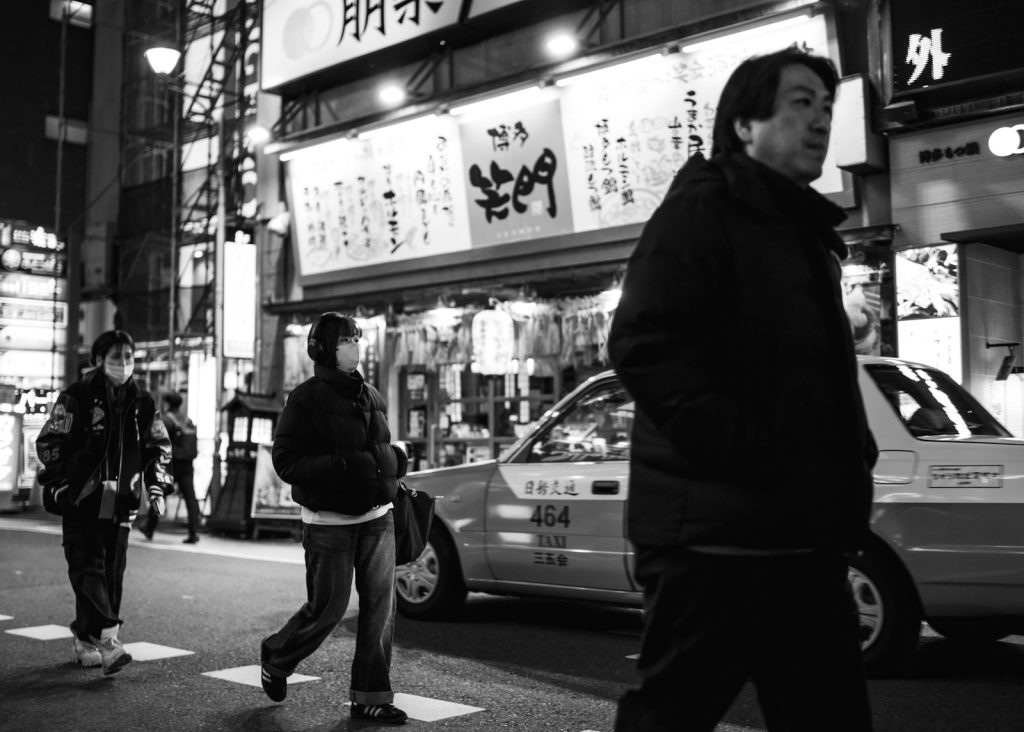 People cross a busy street at night in japan.
